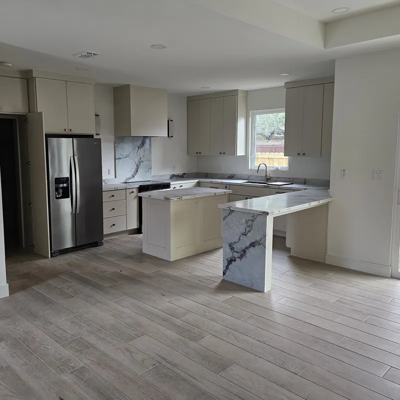 Photograph of the finished kitchen of the same home, with a stone waterfall peninsula.