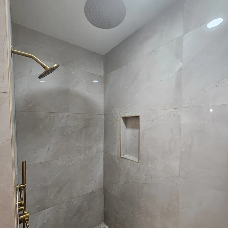 Photograph of a finished shower with large tiles, a niche and brass fittings.
