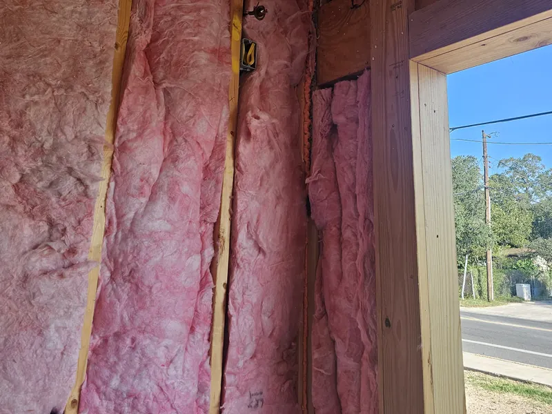 Photograph of insulation fitted between the wall studs beside a window opening.